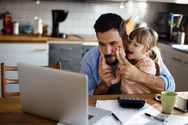Mann mit Kind vorm Laptop beim Home Office